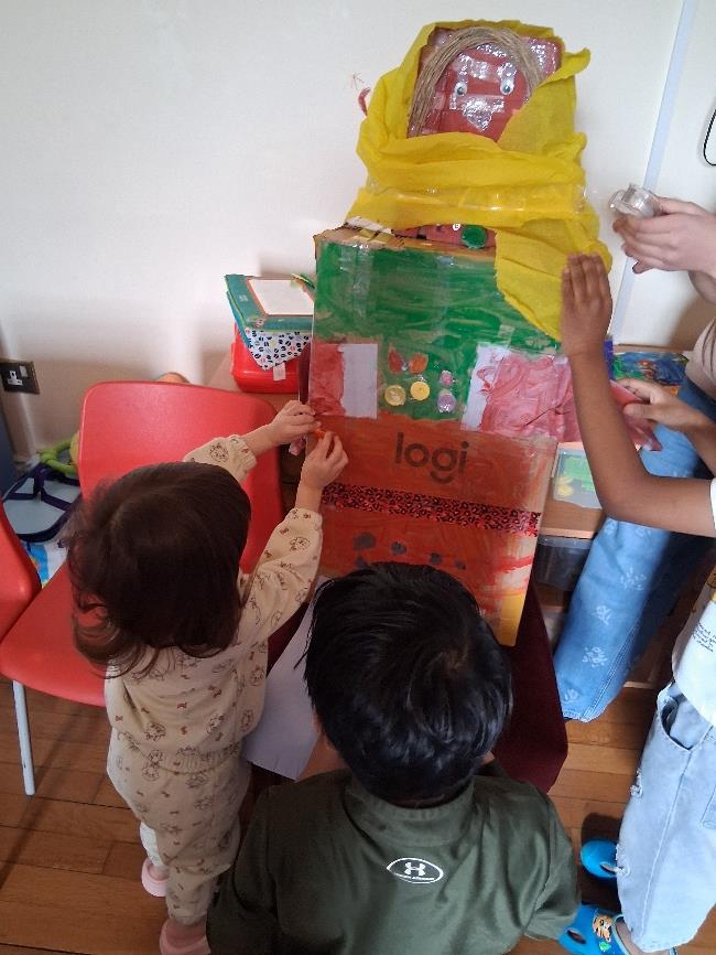 Children at a table working together to dress the tall cardboard figure in yellow fabric and colourful decorations.